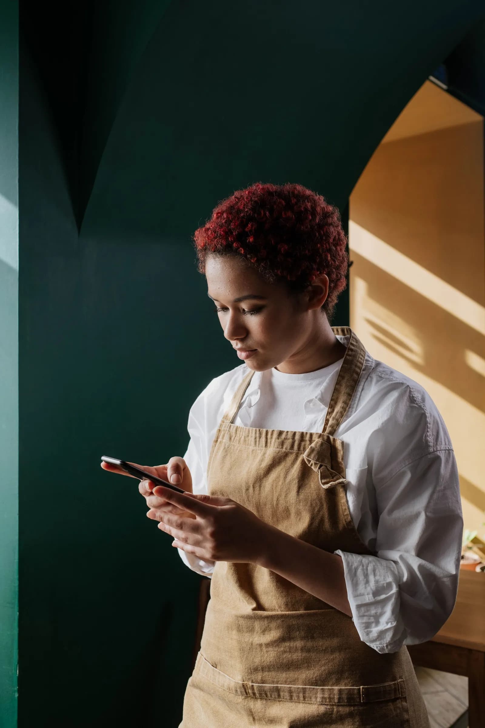 A chef in an apron checking her phone in a warmly lit kitchen